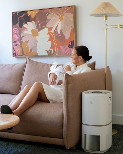 Woman in the sofa next to an Electrolux air purifier.